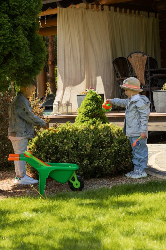 Two children play with gardening tools in a backyard, enjoying the sunny weather.